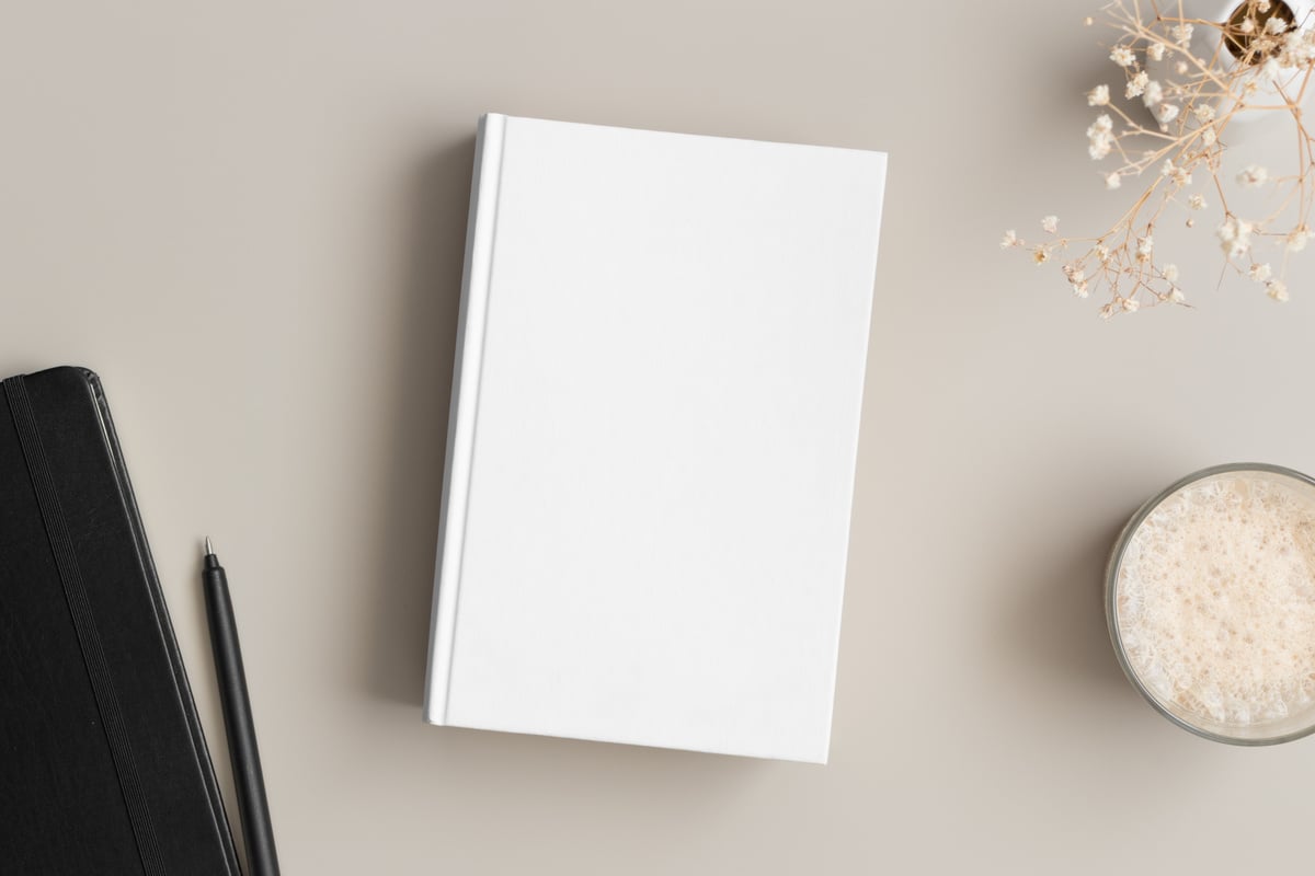 White book mockup with a gypsophila, coffee and workspace accessories on a beige table.